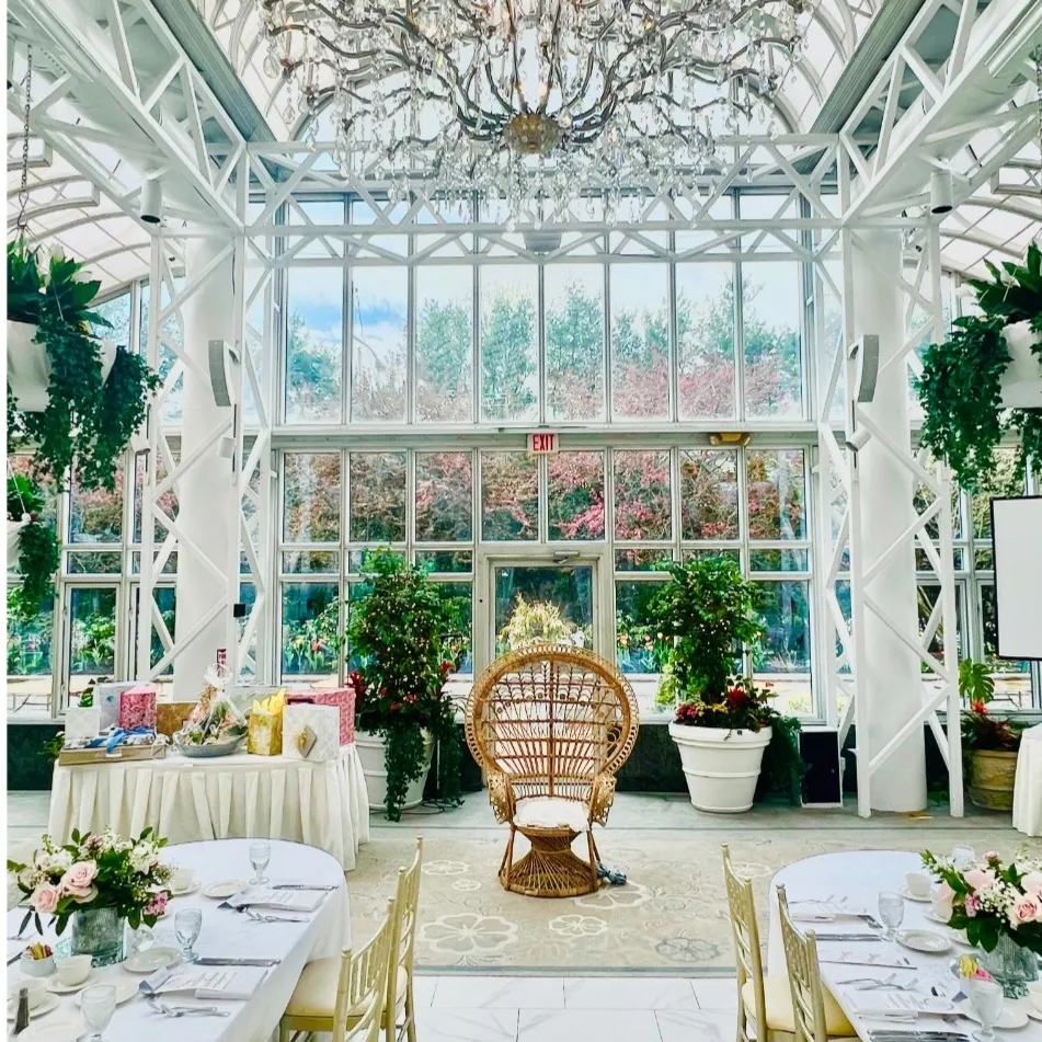 Elegant indoor garden venue on Long Island with crystal chandelier, gold chiavari chairs, white linen tables, floral centerpieces, and a rattan peacock chair for a kids birthday party or special event